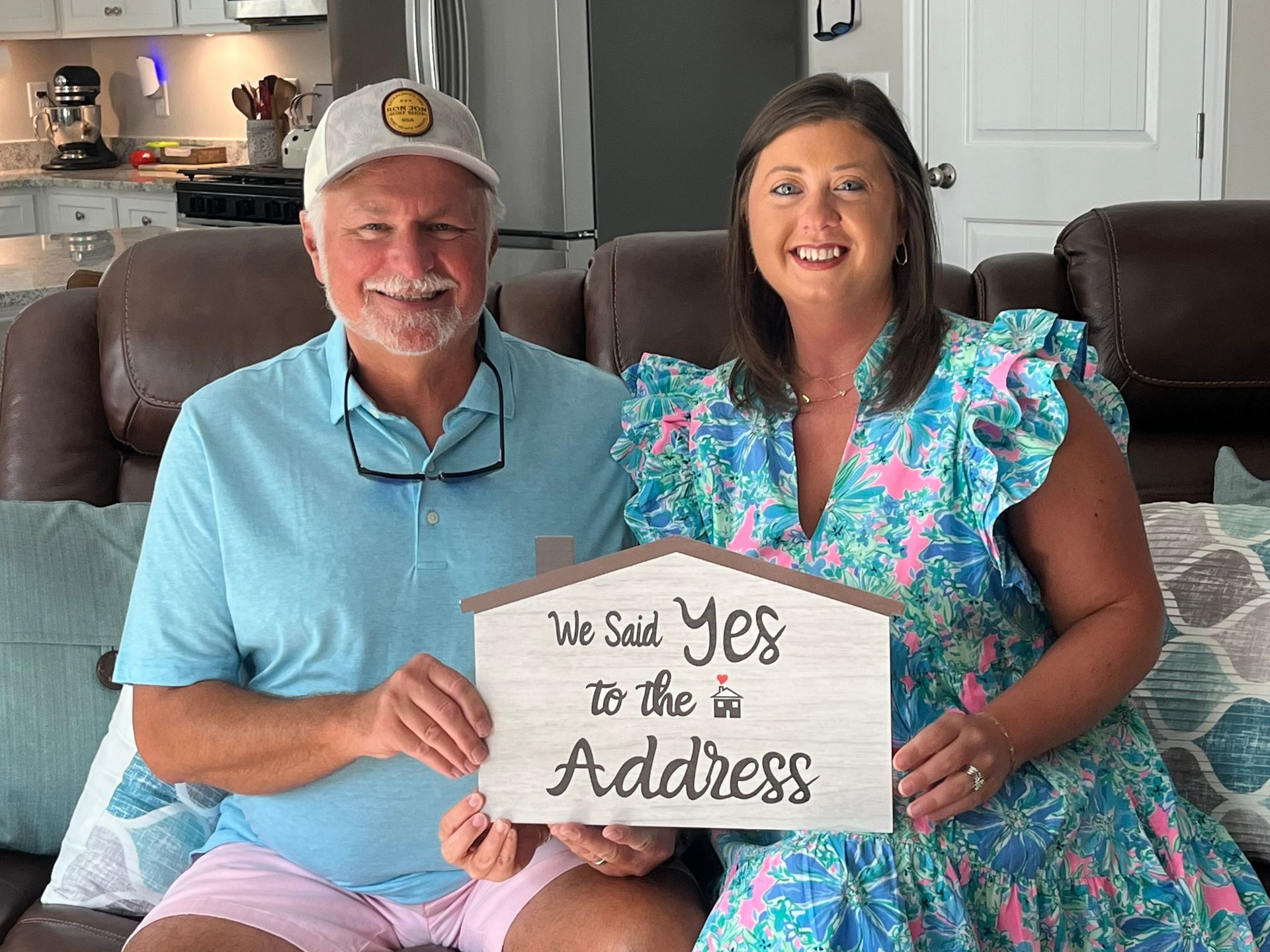 A man and a woman are sitting on a couch holding a sign that says `` we said yes to the new address ''.