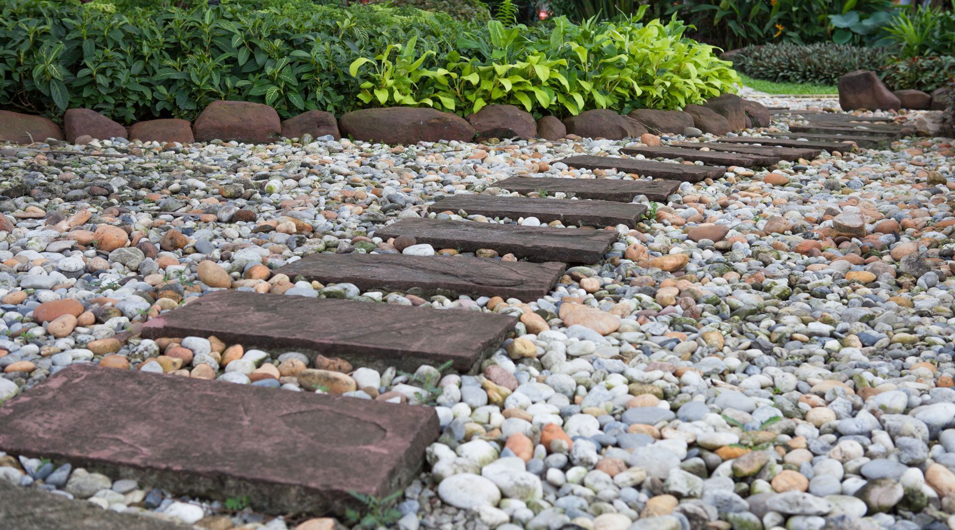 Stepping stones through a gravel path, leading to a lush garden.