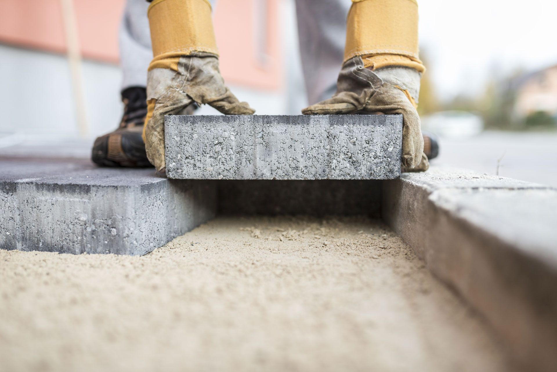 Person in work gloves placing a gray brick onto a sand-filled trench.