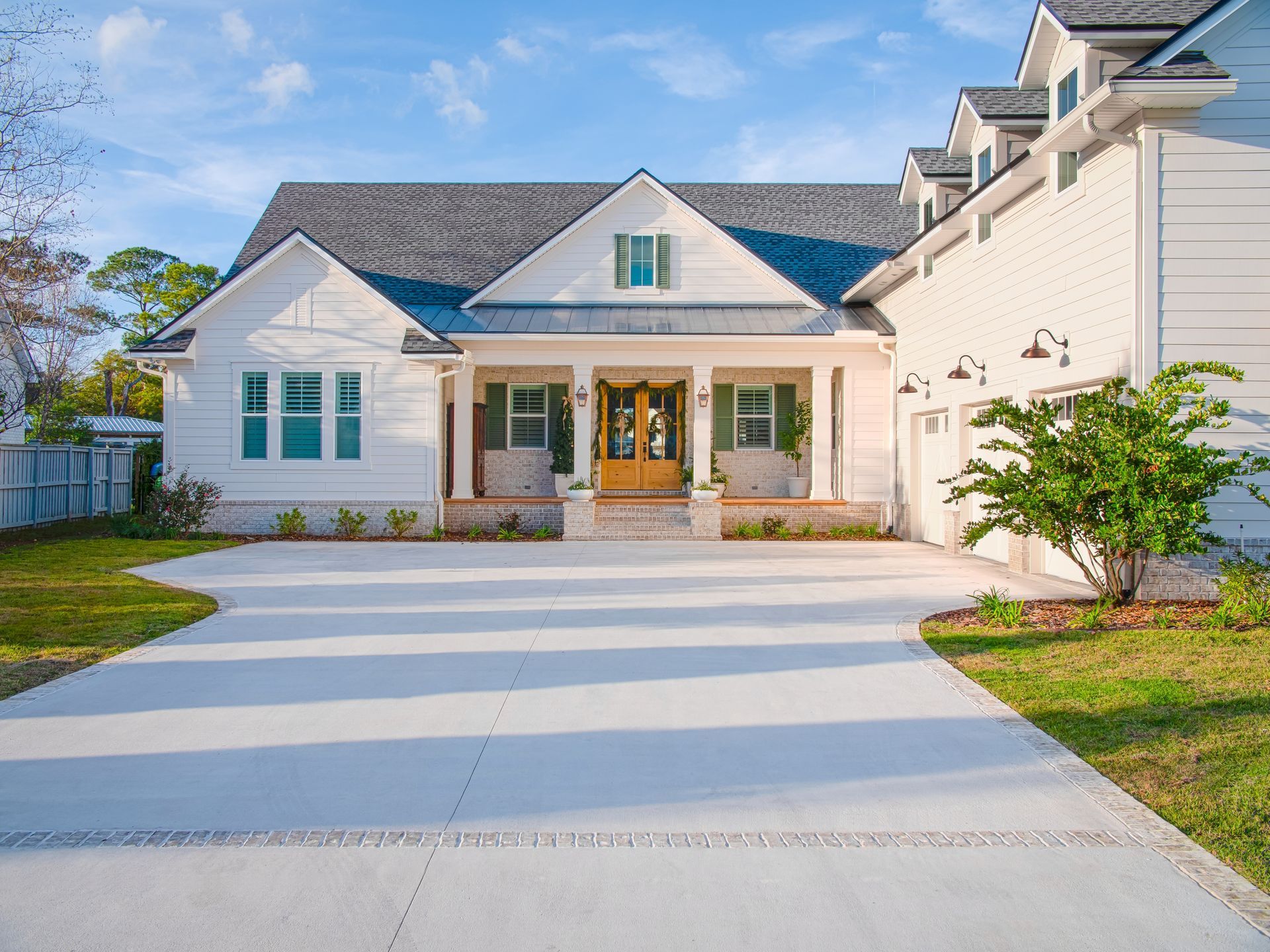 White house with a gray roof, porch, and attached garage; light-colored driveway, blue sky.