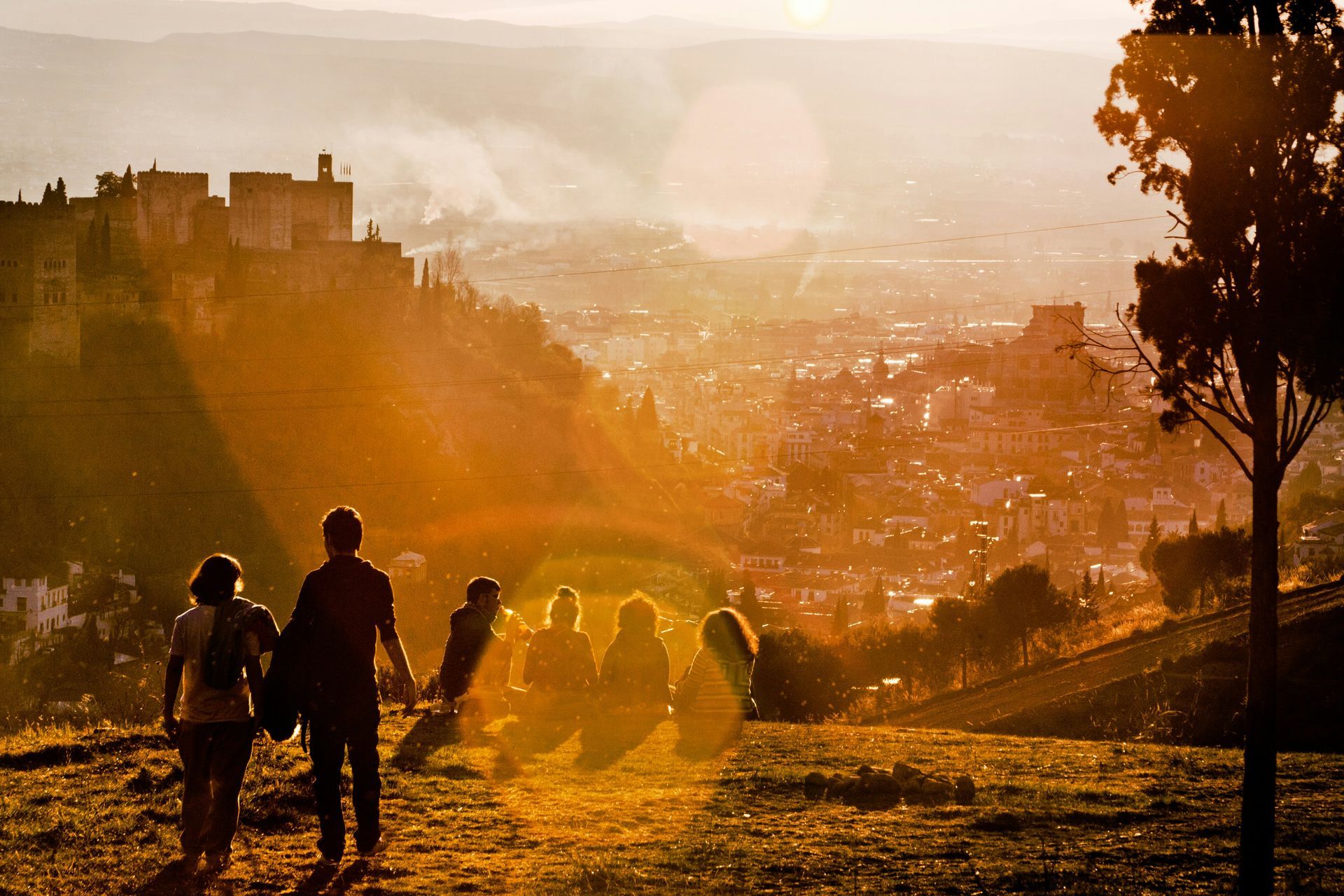 People enjoying a sunset view of the Alhambra in Granada, Spain; Warm golden light bathes the city.