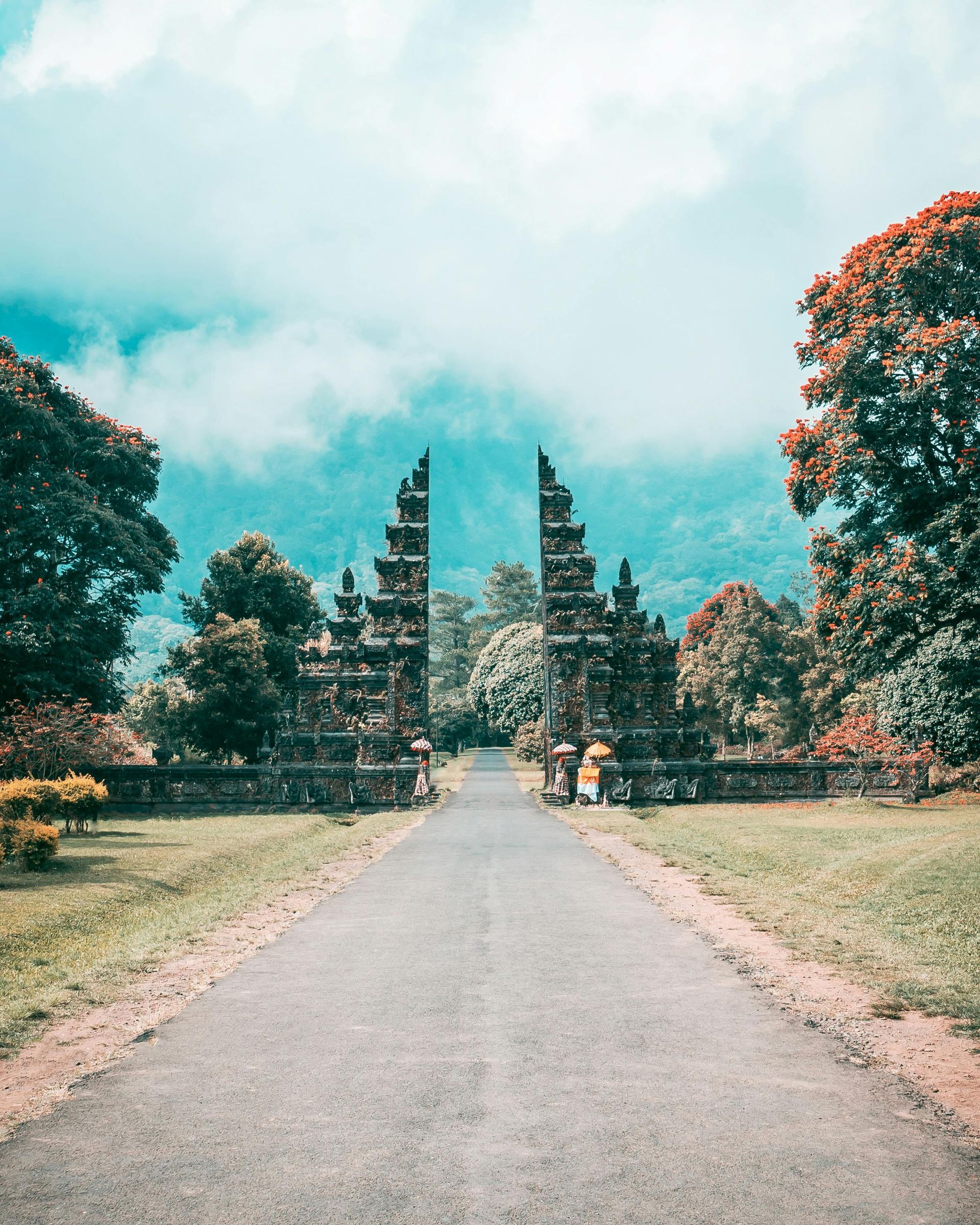 Stone Balinese temple gates frame a road leading toward a misty mountain.