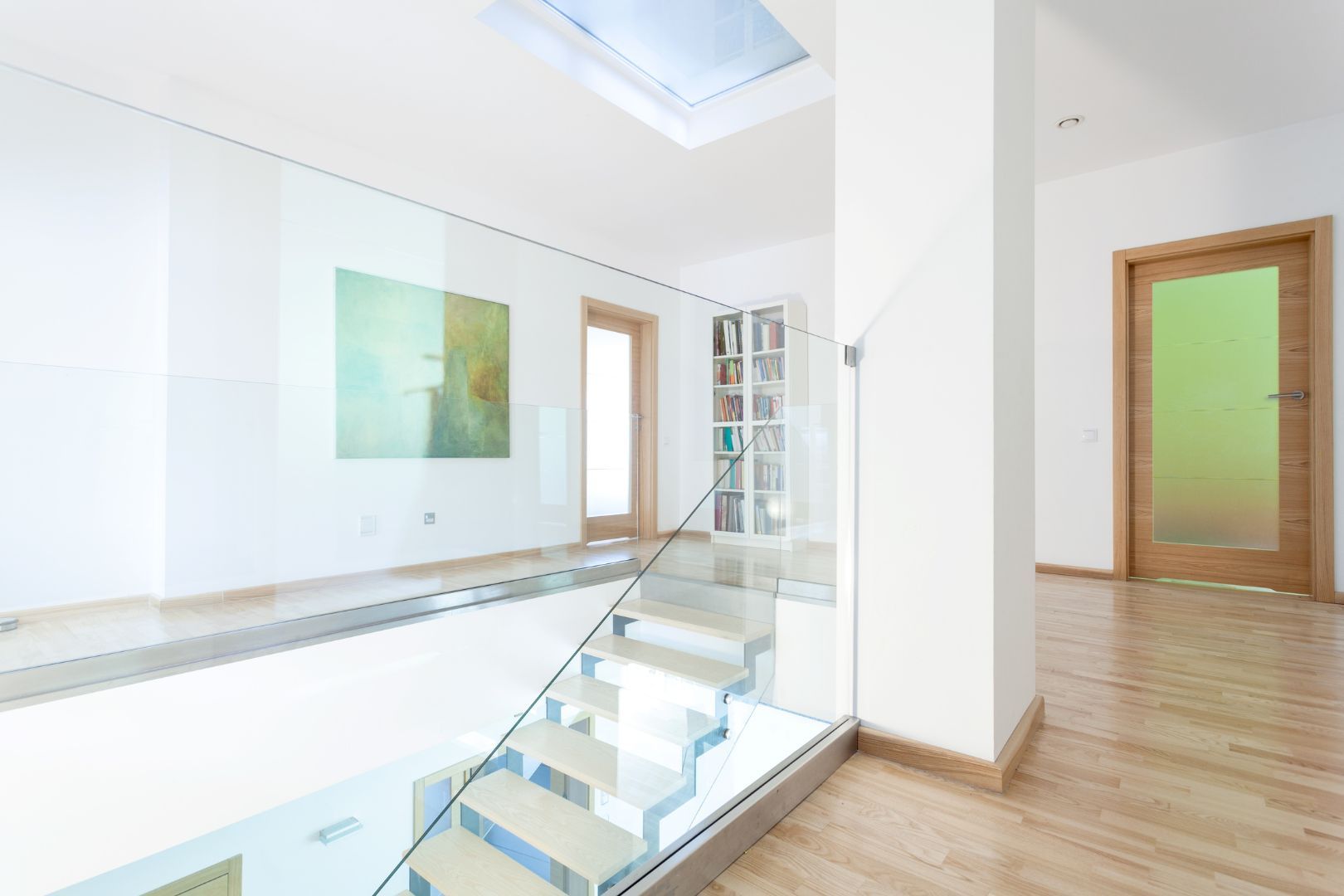 Glass staircase in a home with wooden floors and white painting on the walls and supporting posts.
