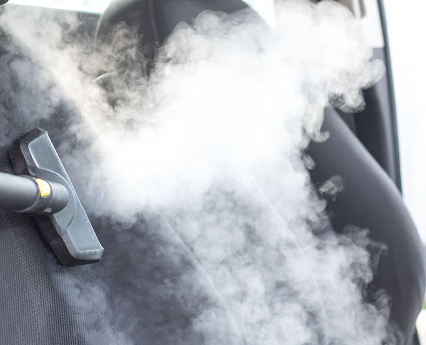 Steam cleaner being used on a car seat, releasing a cloud of steam.