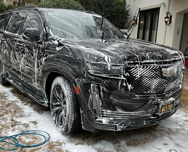 Black Cadillac SUV covered in soap suds, being washed outside in Dallas TX.
