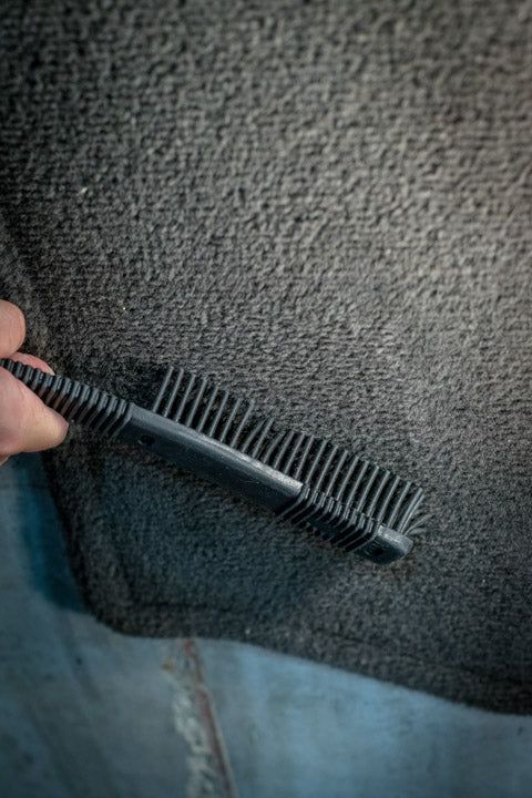 Person holding a black brush removing pet hair from gray carpet.