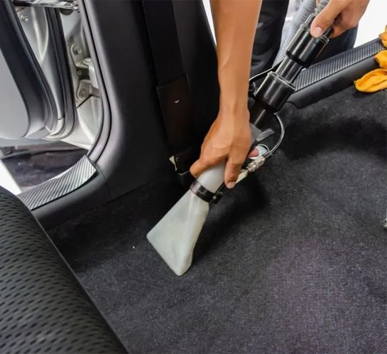 A person vacuuming a car's carpeted interior with a high quality liquid extractor.