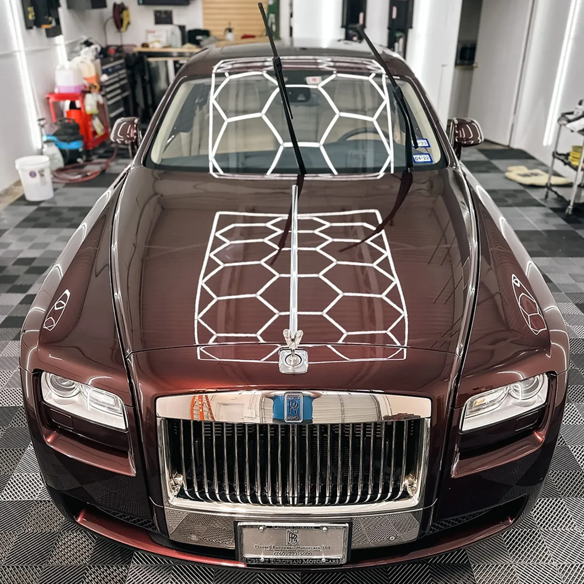 A shiny brown Rolls-Royce with a grid pattern on the hood and windshield in a garage with nano ceramic coating.