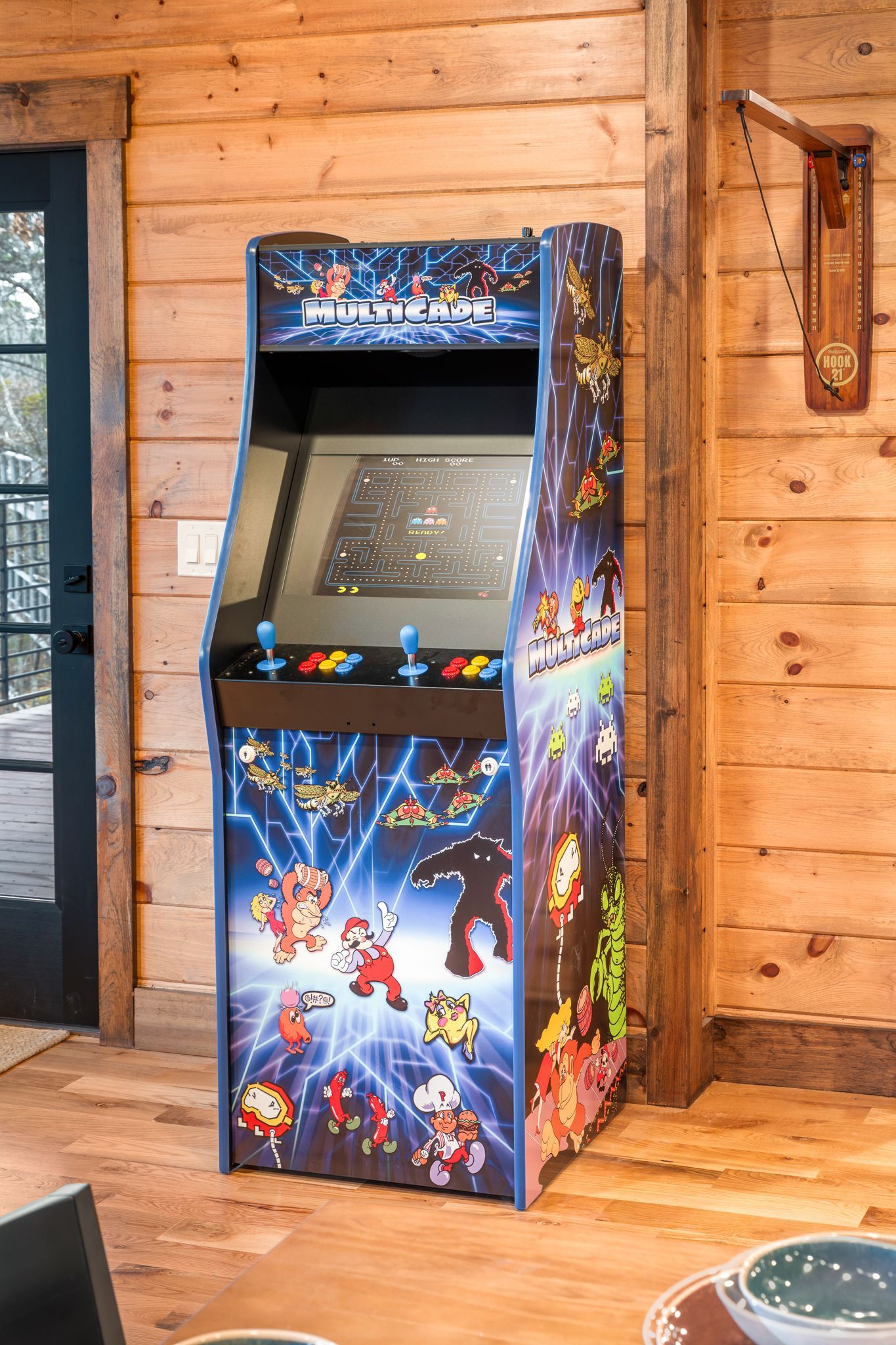A vertical arcade machine with colorful character graphics stands in a room with wood-paneled walls.