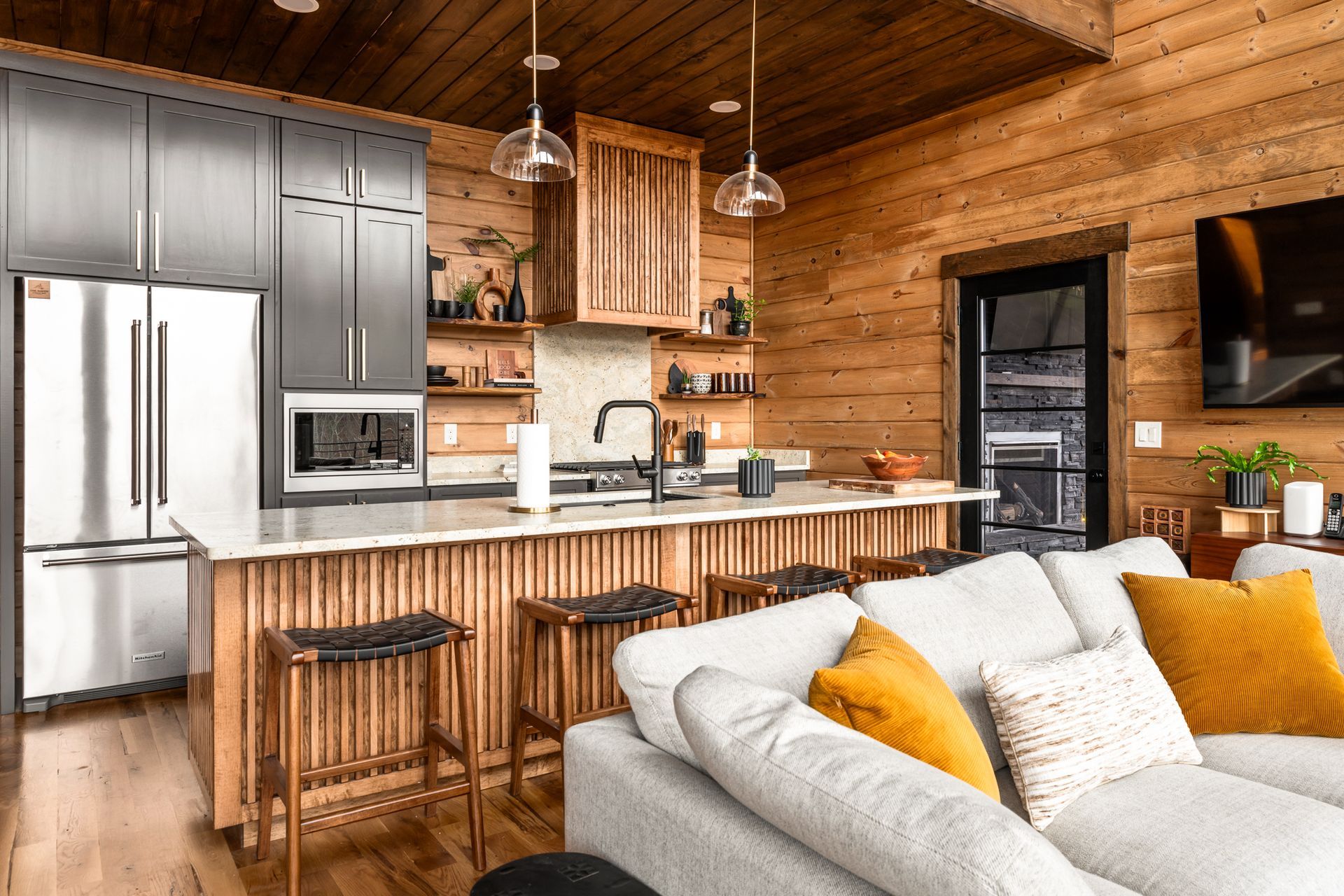 A modern kitchen with wood walls, dark cabinets, and a white island, viewed from an adjacent gray sectional sofa.