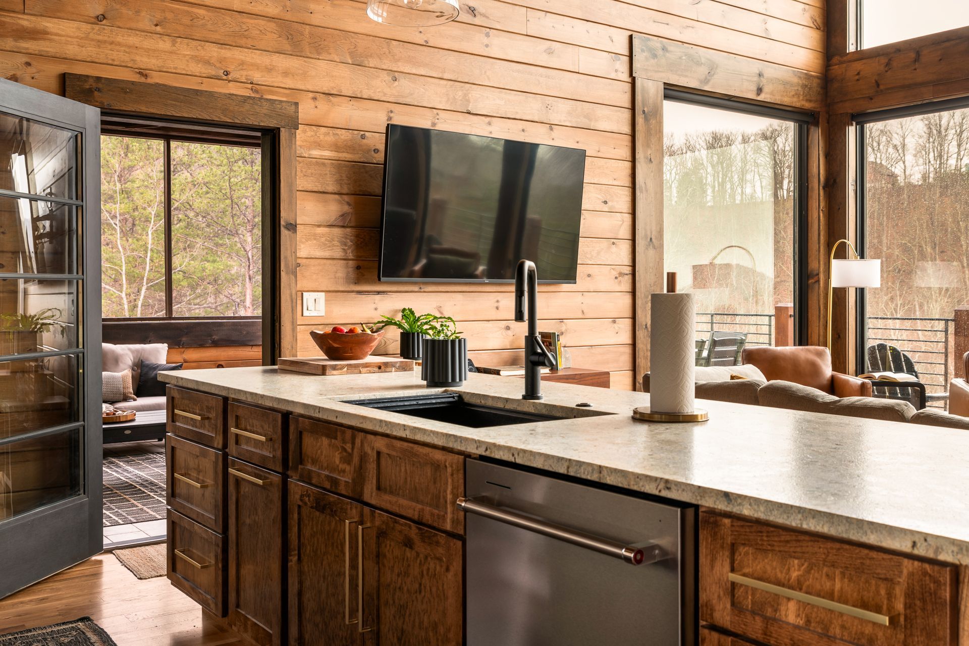 A modern rustic kitchen island with dark wood cabinets, a stone countertop, a sink, and a stainless steel dishwasher.