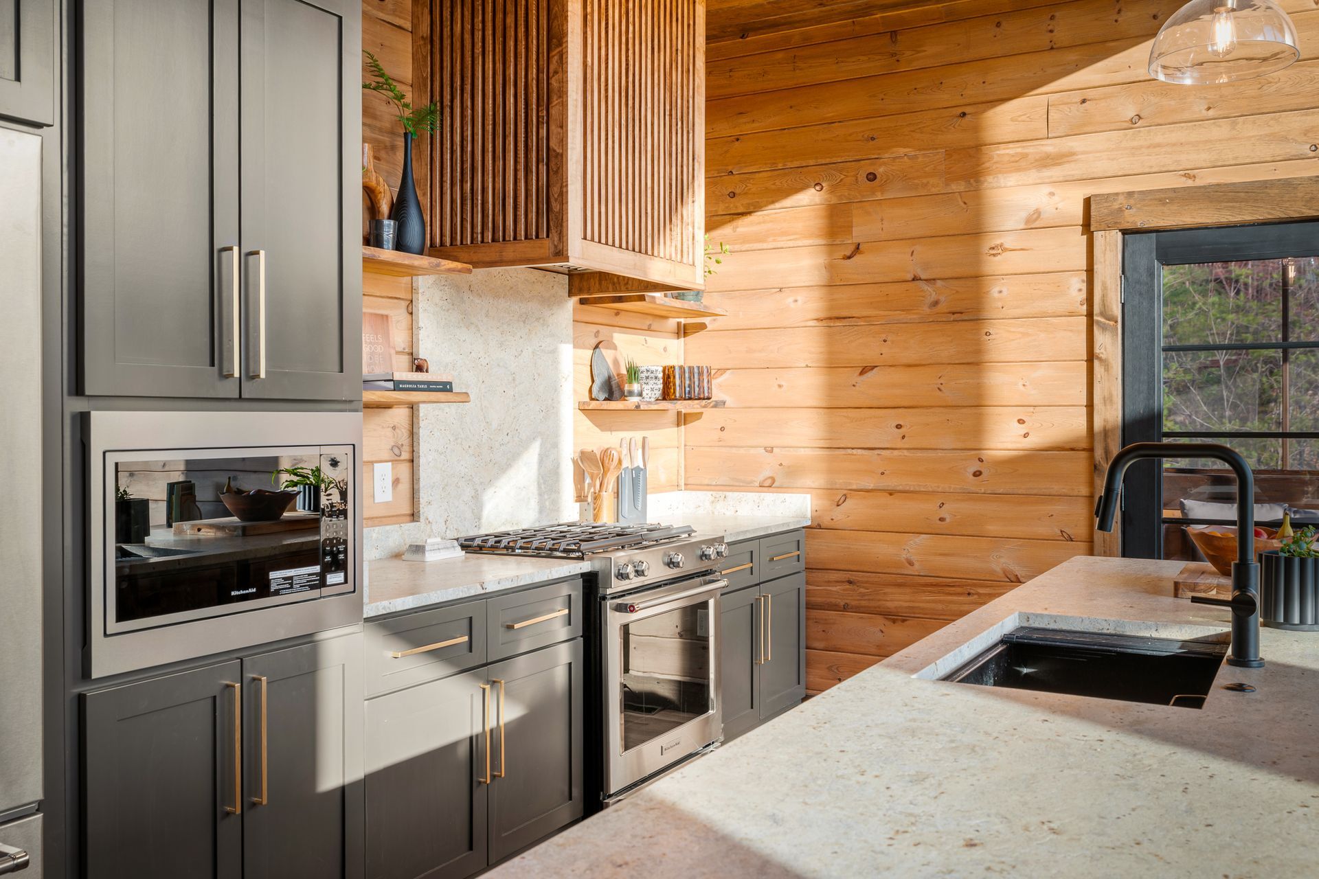 Modern kitchen with dark grey cabinets, light speckled countertops, and stainless steel appliances against wood walls.