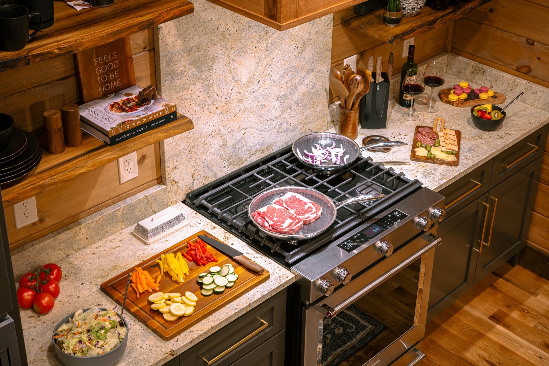 A kitchen counter with a gas stove cooking meat and onions, beside a cutting board of chopped vegetables and a salad bowl.