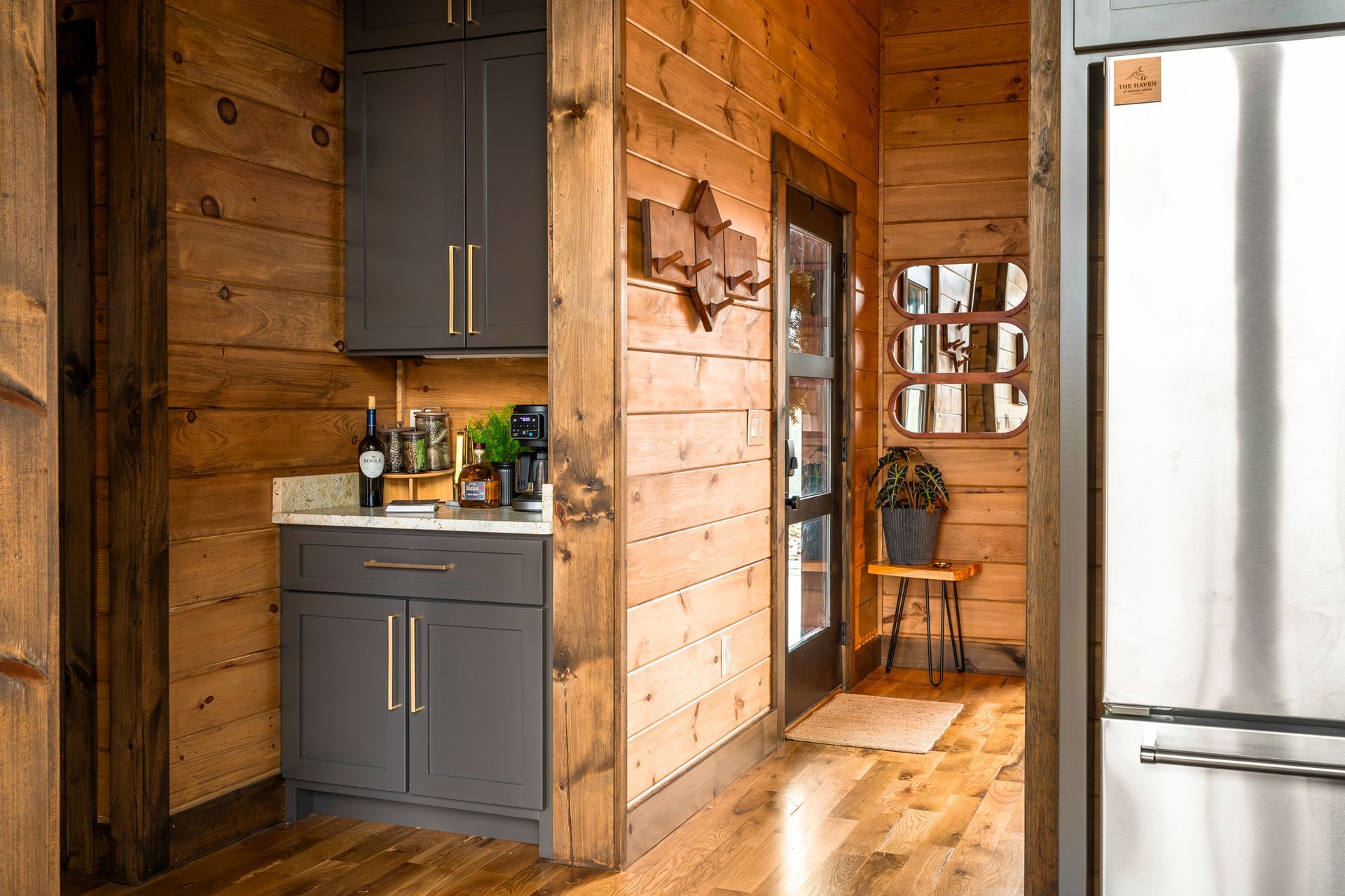 A dark gray kitchen cabinet unit built into a rustic log cabin wall, next to a stainless steel refrigerator.