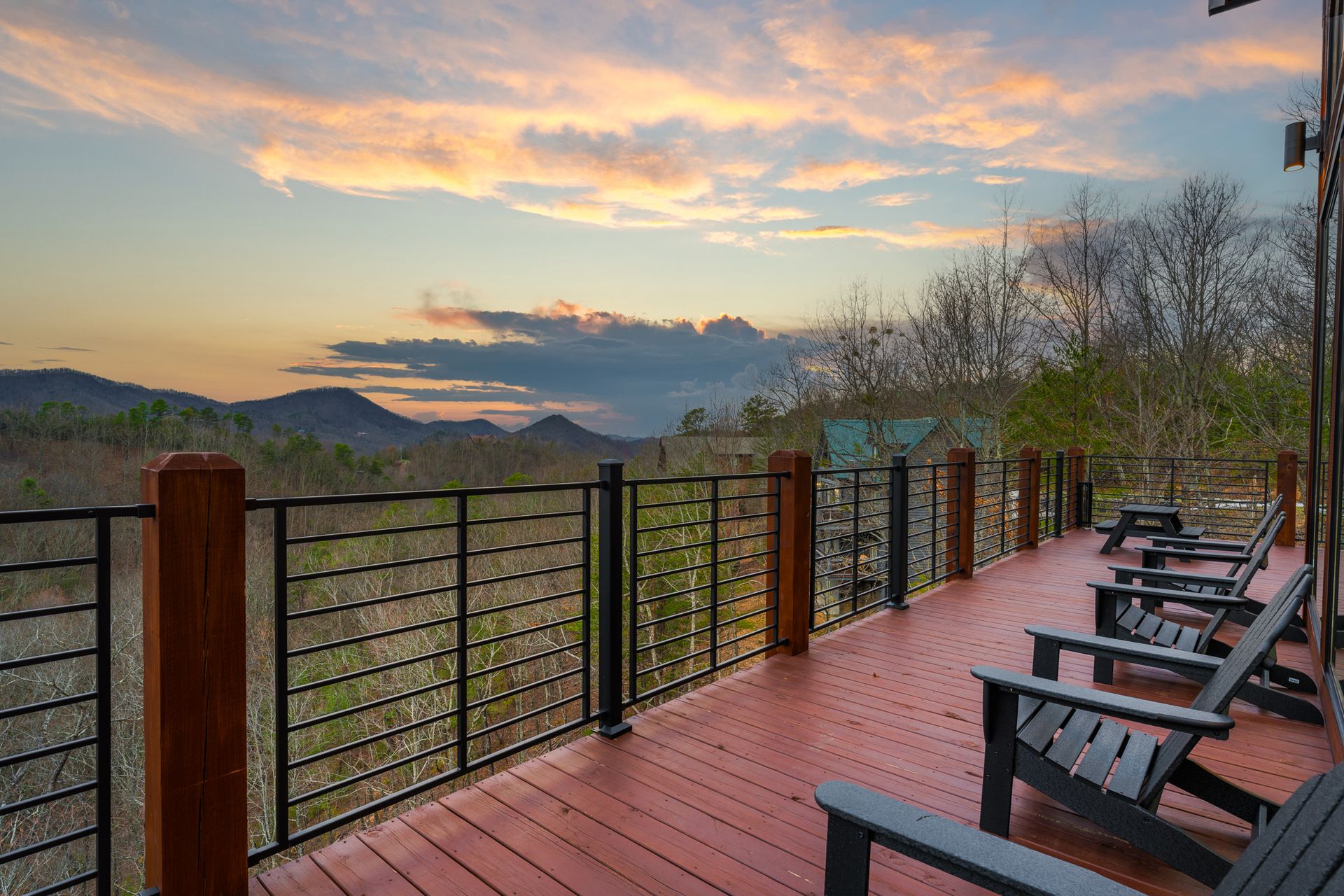 A wooden deck with black chairs overlooking a mountain range during a colorful sunset.