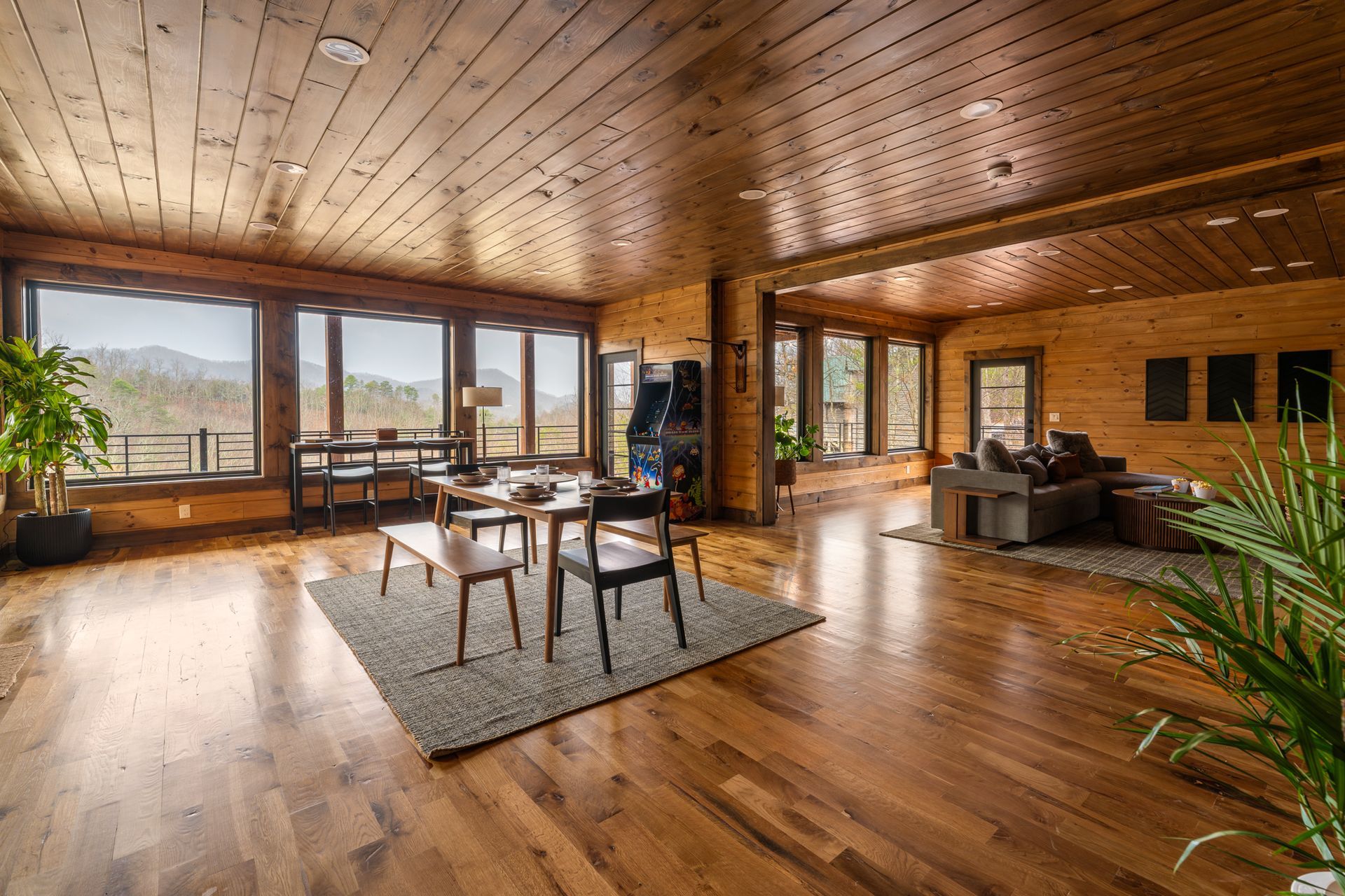 A spacious, rustic log cabin living area with wooden walls and ceilings, a dining set, and a view of mountains.