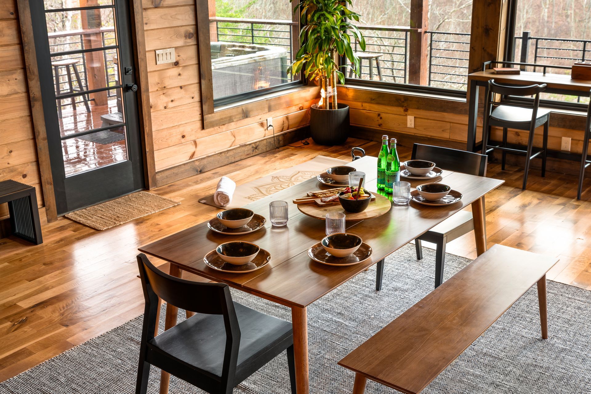 A wood-paneled dining room with a table set for four, featuring black chairs, a bench, and a nearby houseplant.