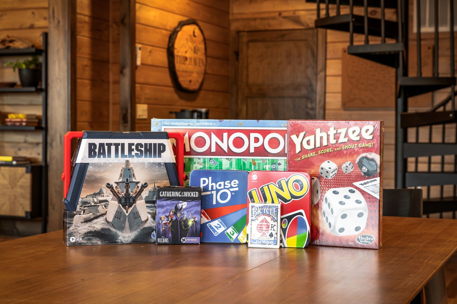 A collection of board and card games, including Monopoly, Battleship, and Yahtzee, arranged on a wooden table.