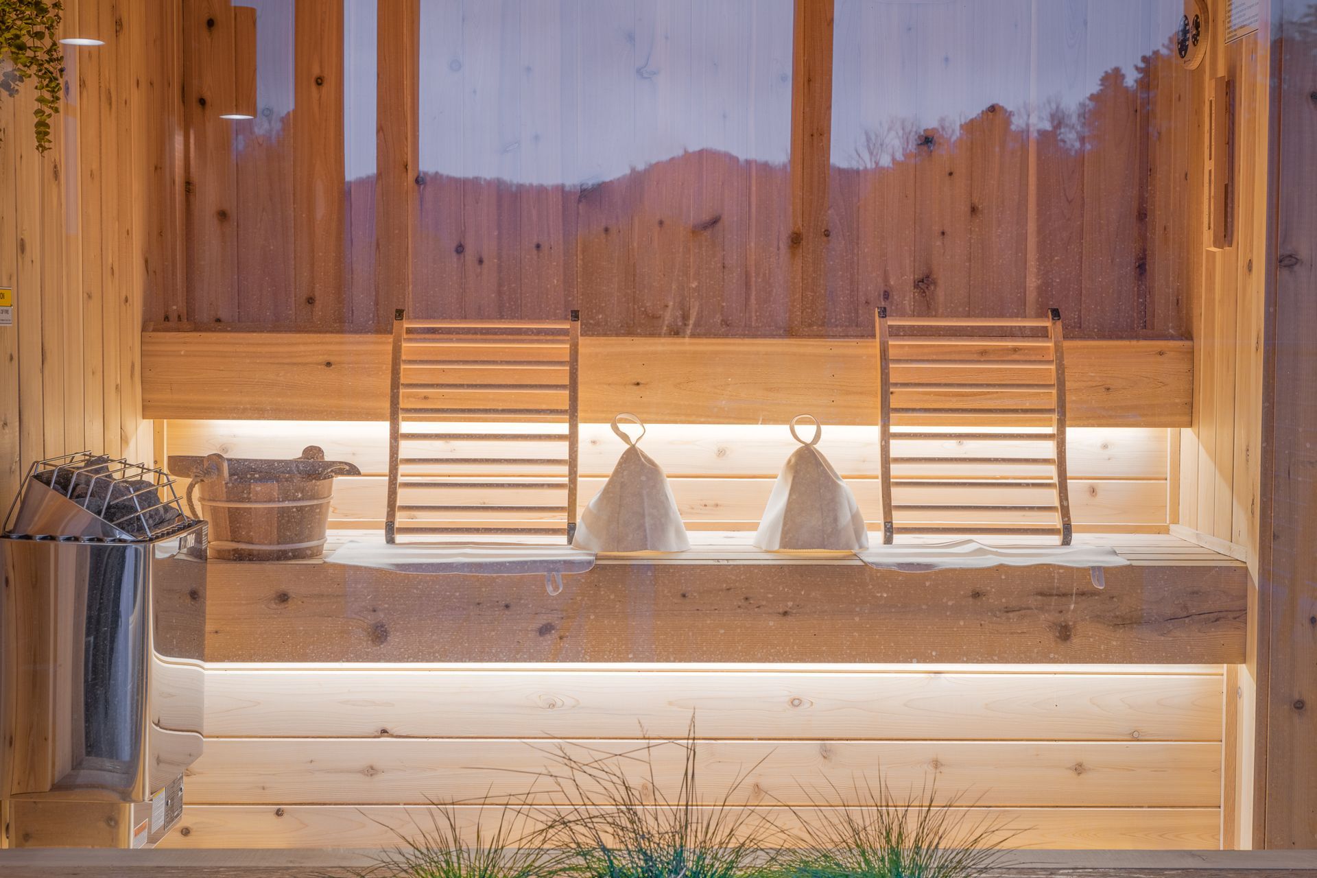 A bright wooden sauna featuring two ladder-style headrests, white covers, and a heater, with mountain views through glass.