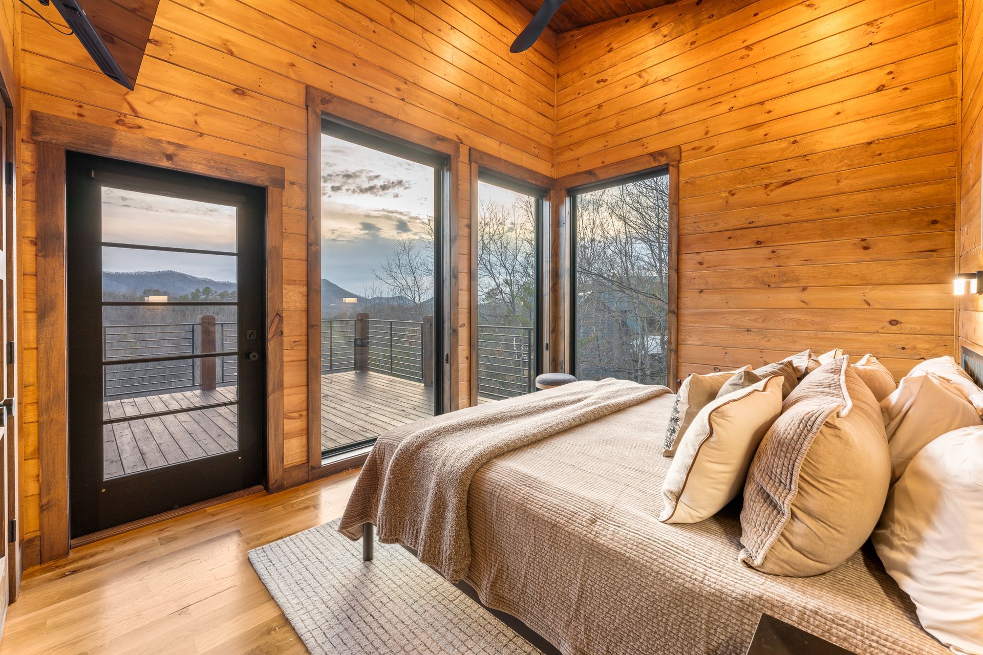 A wood-paneled bedroom with a large bed, light bedding, and expansive windows offering a scenic outdoor view.