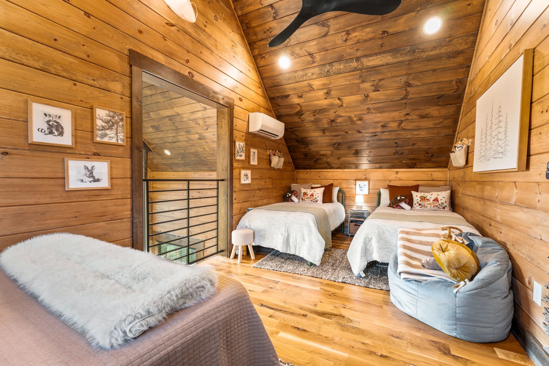 A rustic bedroom in a wooden attic featuring two twin beds, a seating area, and framed wall art.