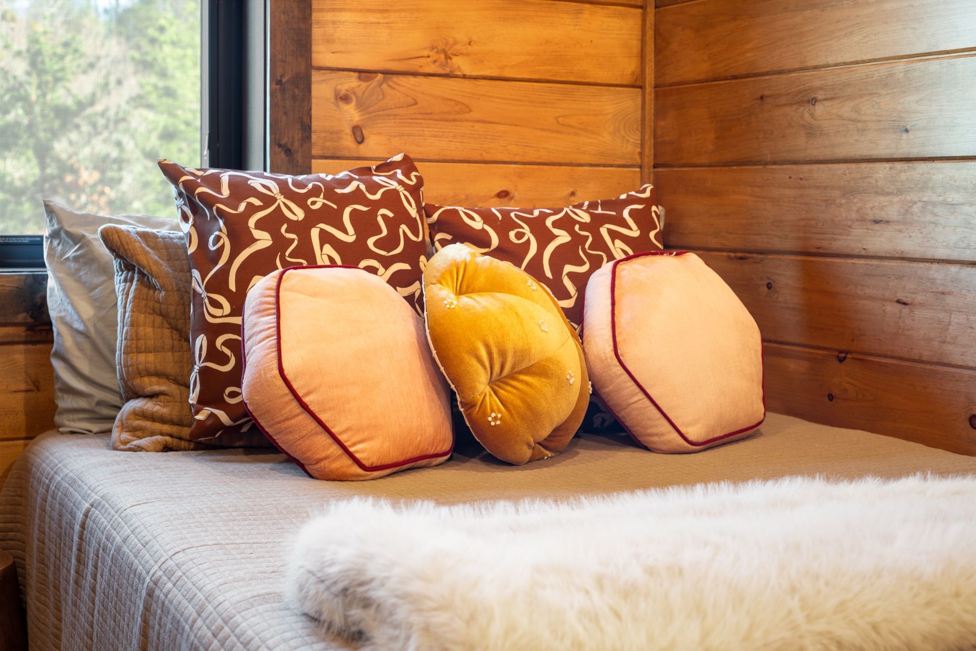 A cozy daybed in a room with wood-paneled walls, featuring decorative throw pillows and a plush white blanket.
