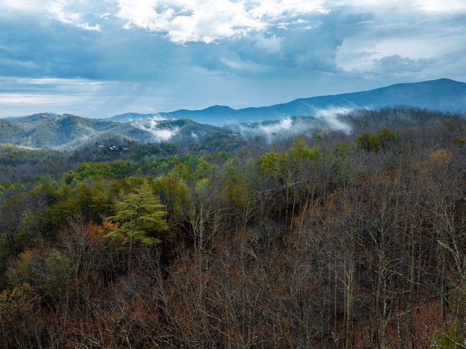 A panoramic view of rolling, tree-covered mountains under a cloudy sky with wisps of mist settling in the valleys.