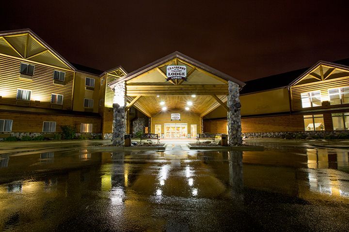 Night exterior of a hotel with a covered entrance, illuminated by lights reflecting on a wet pavement.