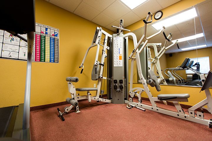 Gym interior with weight machines, a treadmill, mirror, and a workout guide on the wall.