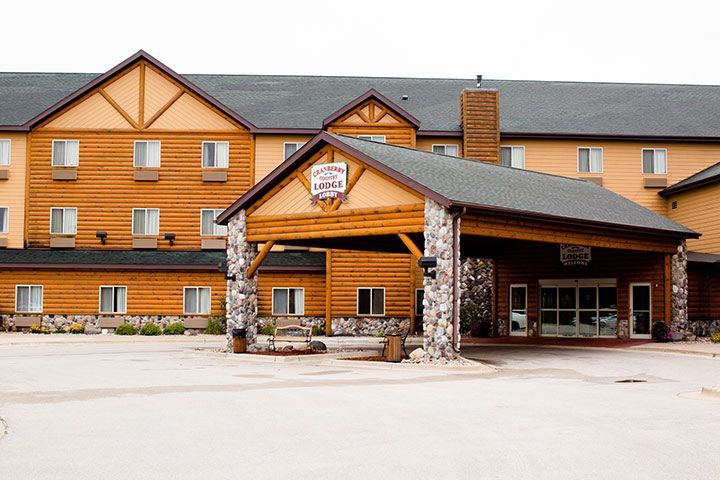 Log-cabin style hotel entrance with stone pillars, covered walkway, and a gray roof.