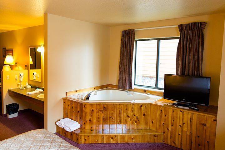 Hotel room with a jacuzzi, TV, window, and a bathroom visible.