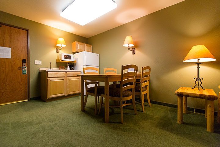 Small hotel room with kitchenette, dining table, and green carpet.