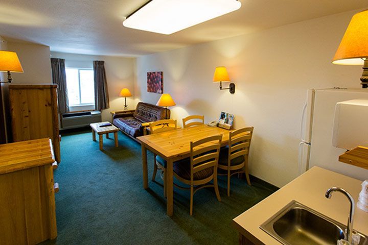 Interior of a hotel room with a kitchenette, dining table, sofa, and two dressers.
