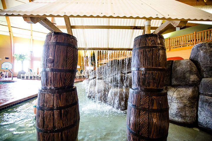 Two wooden barrels frame a waterfall feature in an indoor water park.