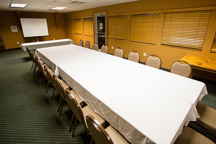 Conference room with long table covered in white cloth, chairs, and projector screen.
