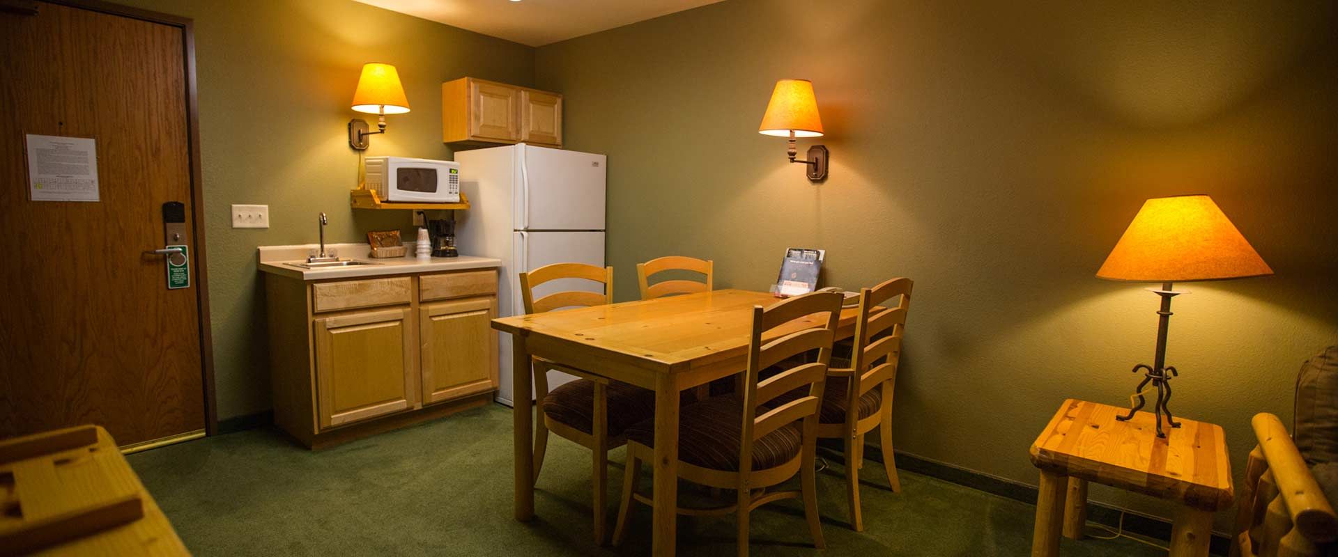 Cozy kitchen and dining area in a lodge. Includes a table and chairs, a fridge, and a lamp.