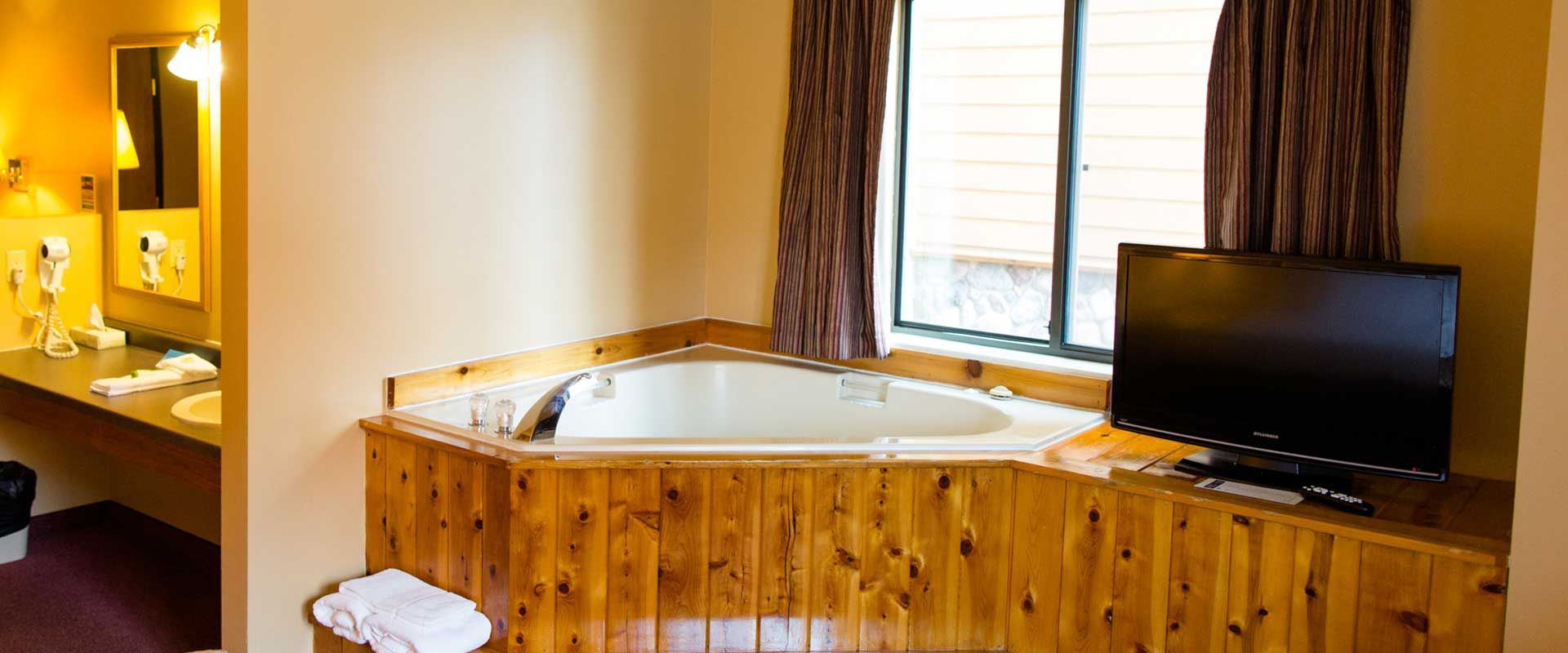 Hotel room with a jacuzzi tub in a wood panel surround and a television.