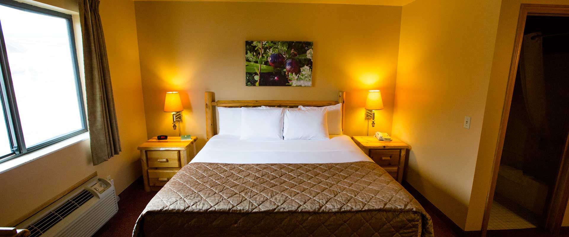 A hotel room with a bed, nightstands, lamps, window, and artwork. Warm lighting and brown tones.