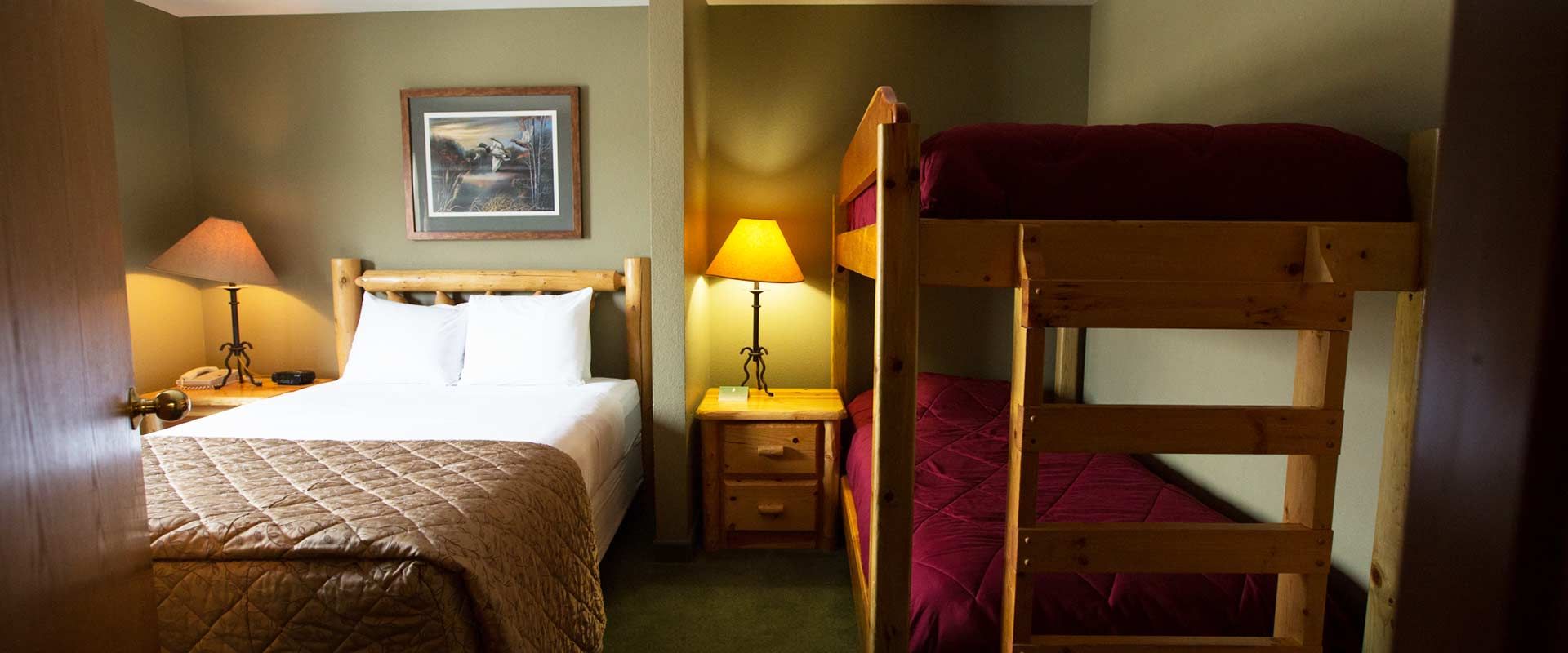A bedroom with a single bed and a bunk bed, both with maroon bedding. Two lamps illuminate the room.