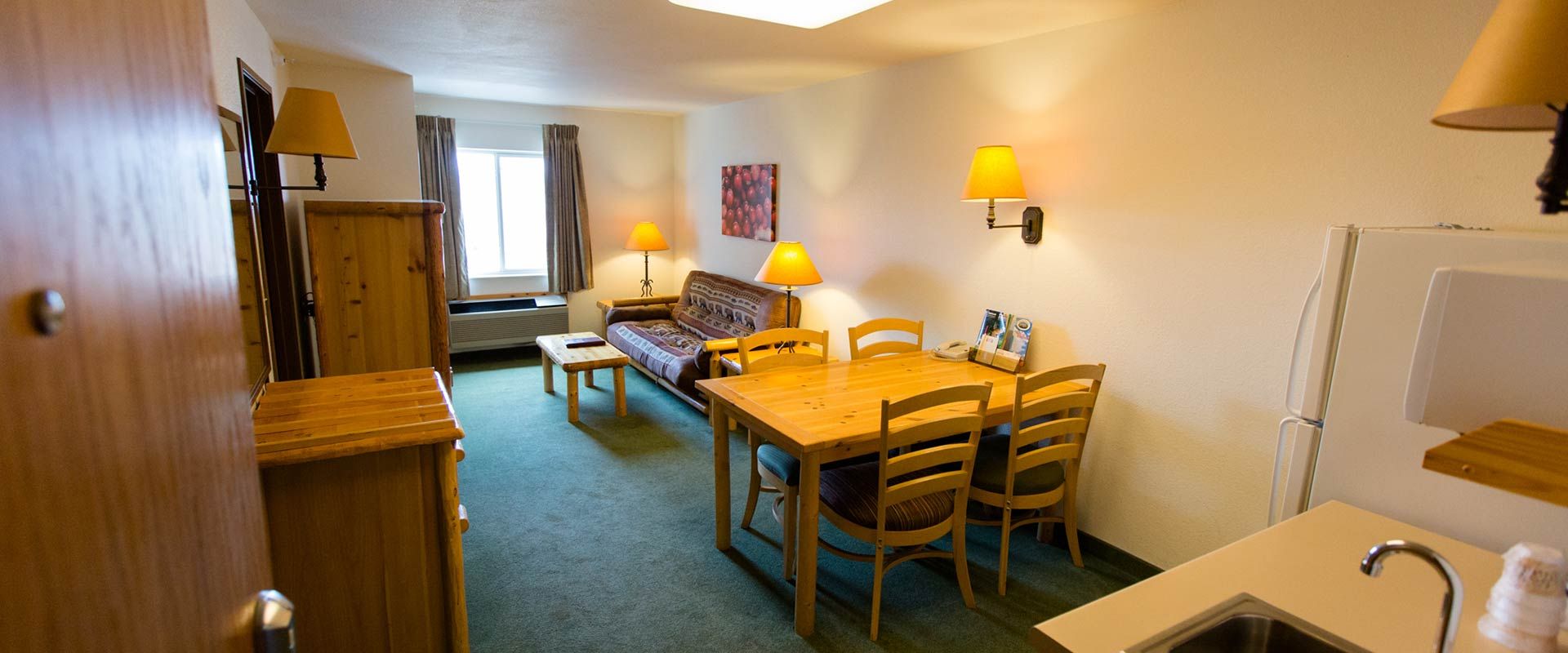 Interior of a hotel room with living area and kitchenette, featuring a dining table and sofa.