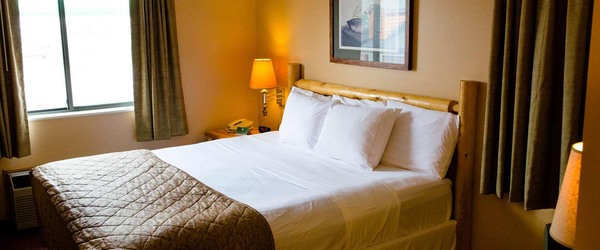 Bedroom with a made bed, lamp, window, and brown curtains.