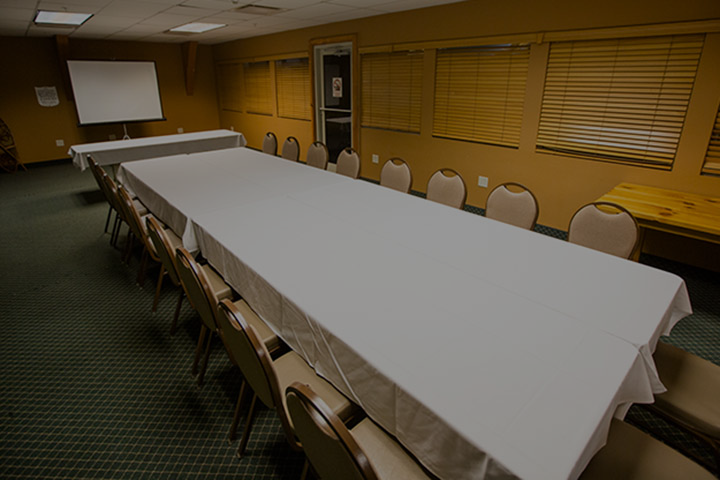 Long conference table set for a meeting with chairs, projector screen, and blinds.