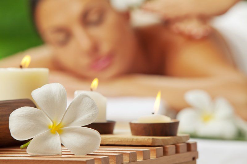 Frau bekommt eine Massage, Spa-Ambiente mit Kerzen, weißen Blumen und sanfter Beleuchtung.