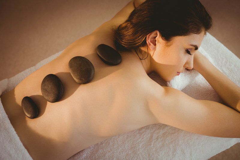 Frau erhält eine Hot-Stone-Massage; Steine auf ihrem Rücken, auf einer Spa-Liege liegend.