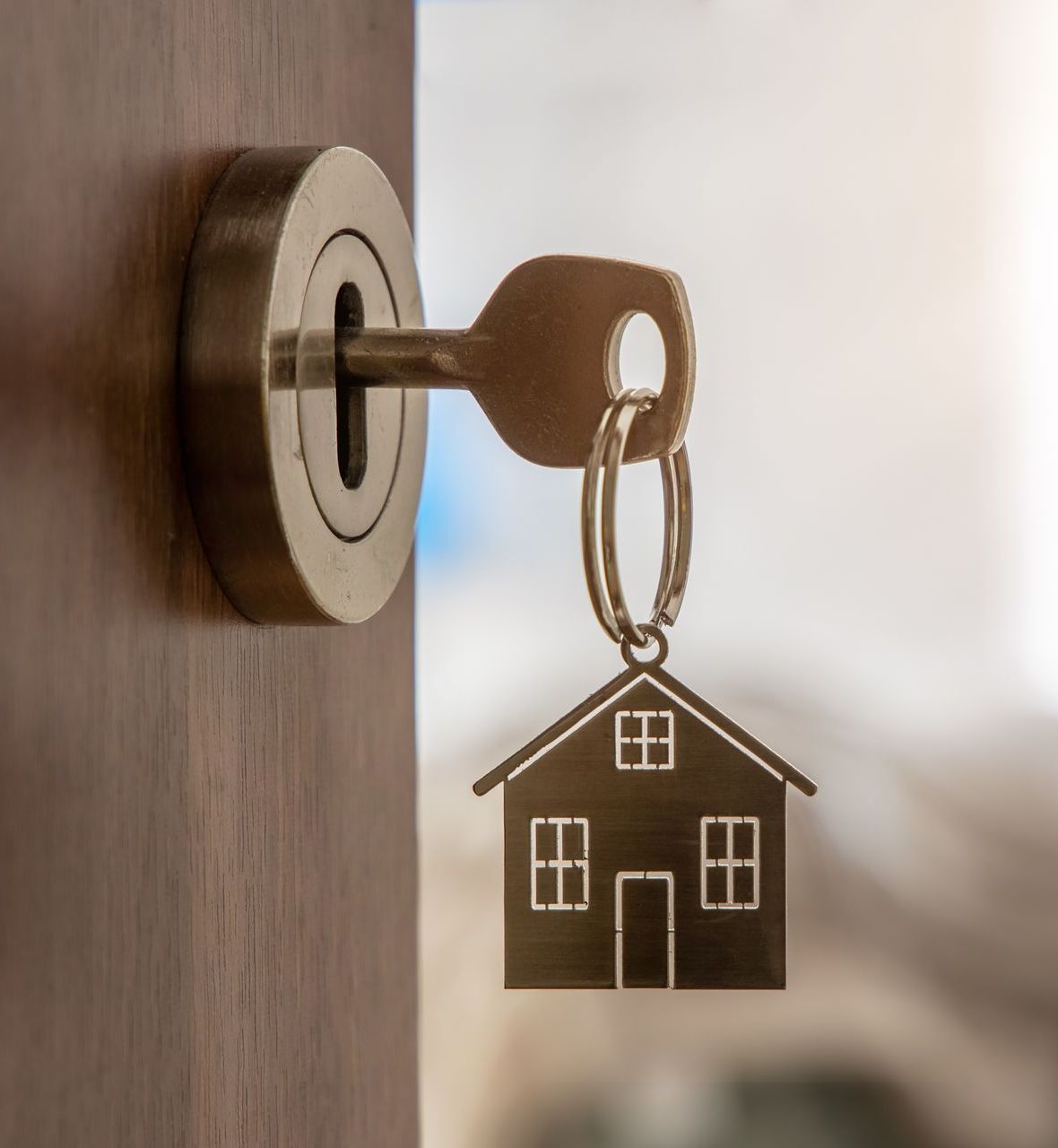 A key in a door lock with a house keychain attached to it.