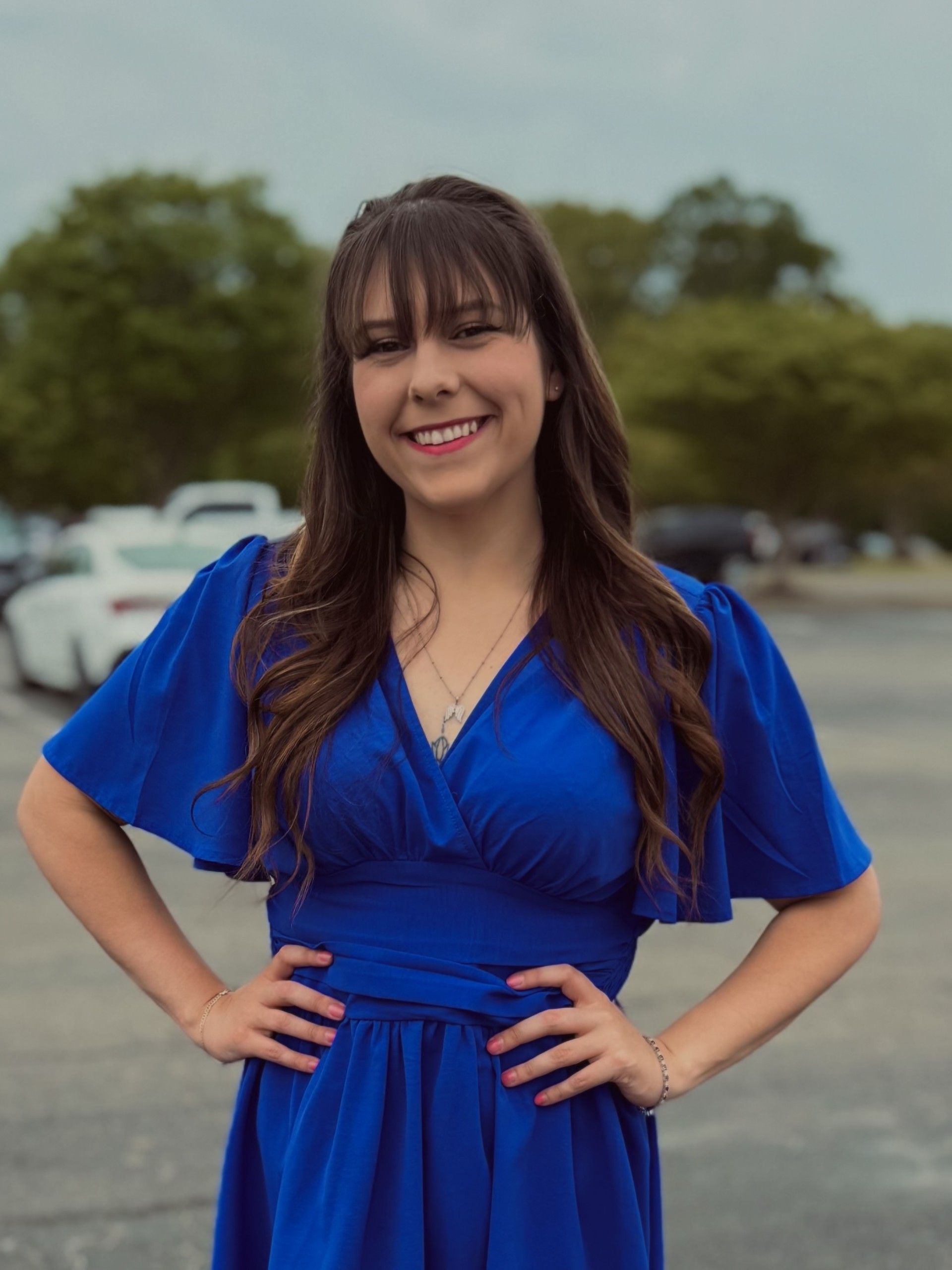 A woman in a blue dress is standing in a parking lot with her hands on her hips.