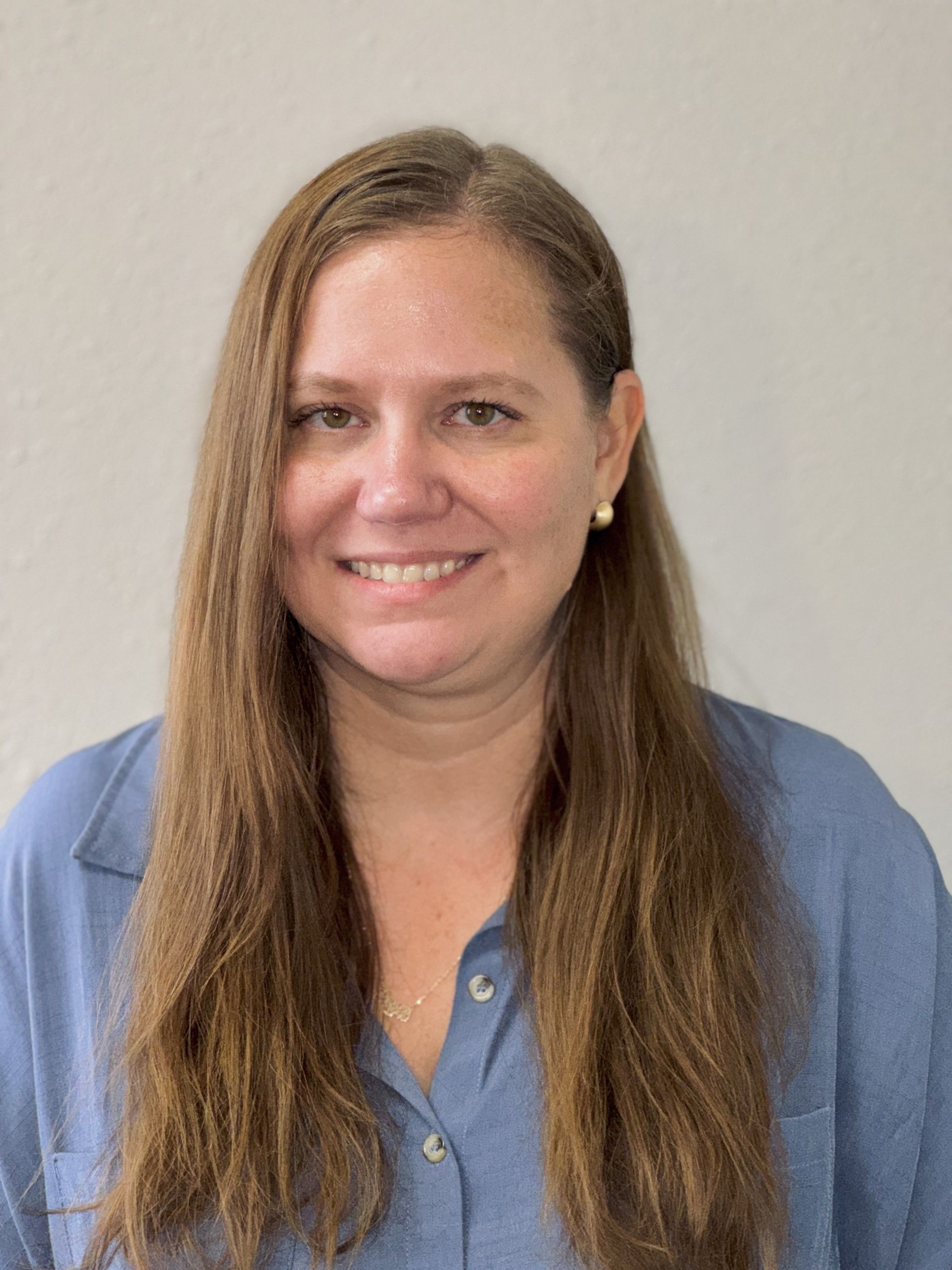 A woman with long hair is wearing a blue shirt and smiling for the camera.