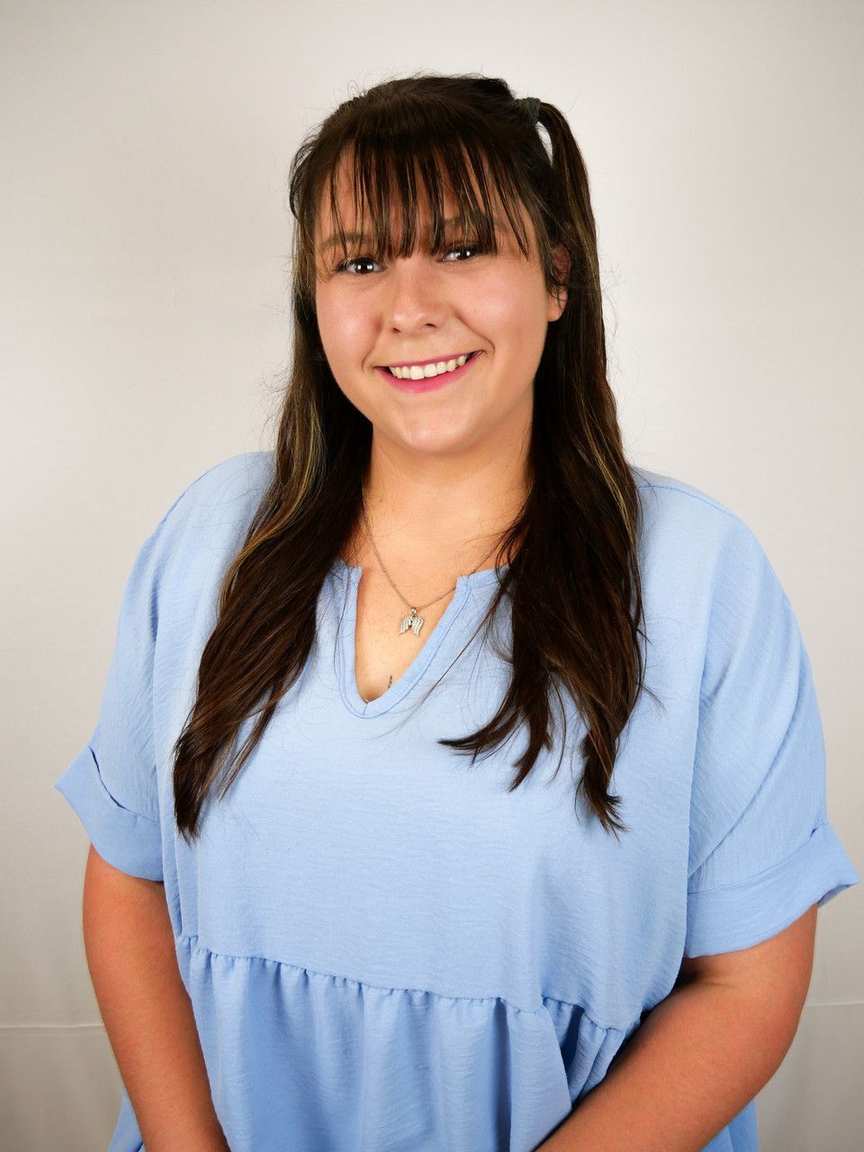 A woman wearing a blue shirt and a necklace is smiling for the camera.