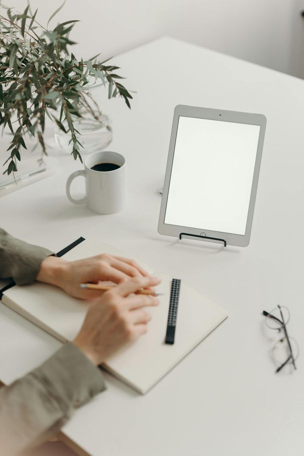 A person is sitting at a desk with a tablet and a notebook.