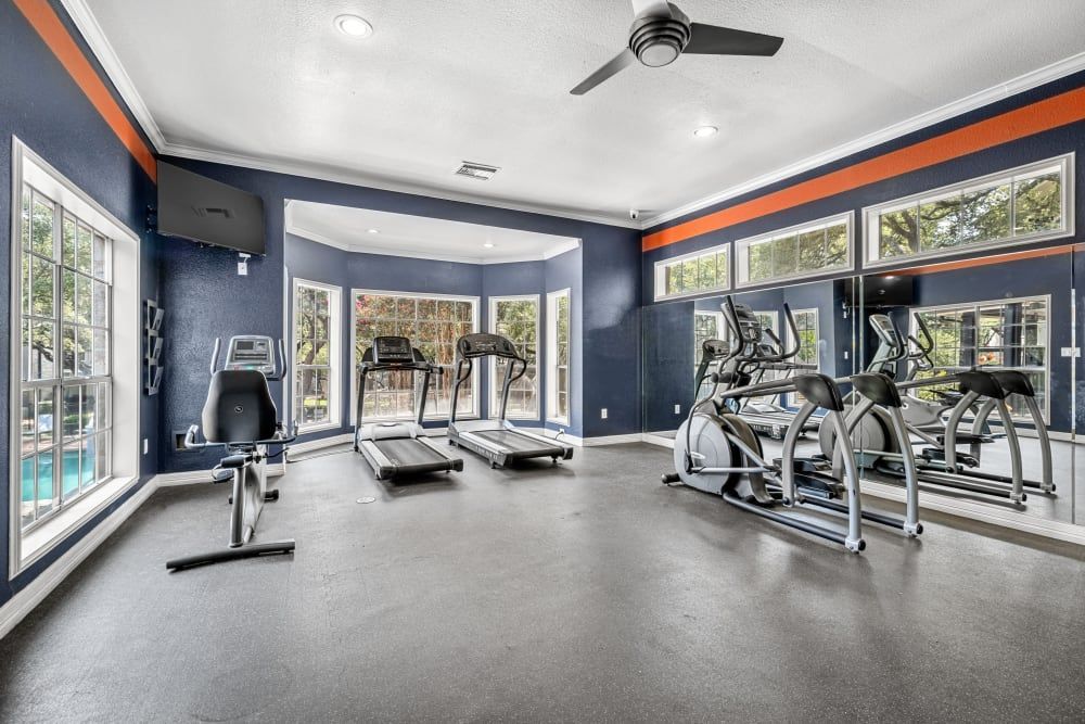 a large gym with treadmills, ellipticals, and a ceiling fan at Marquis at Deerfield in San Antonio, TX.